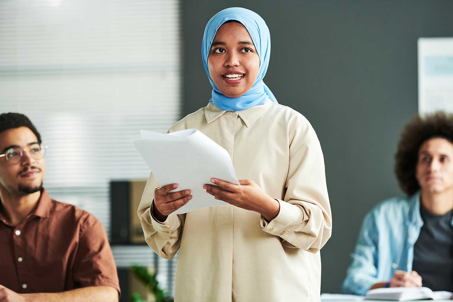 A speaker wearing a hijab stands up to present a report