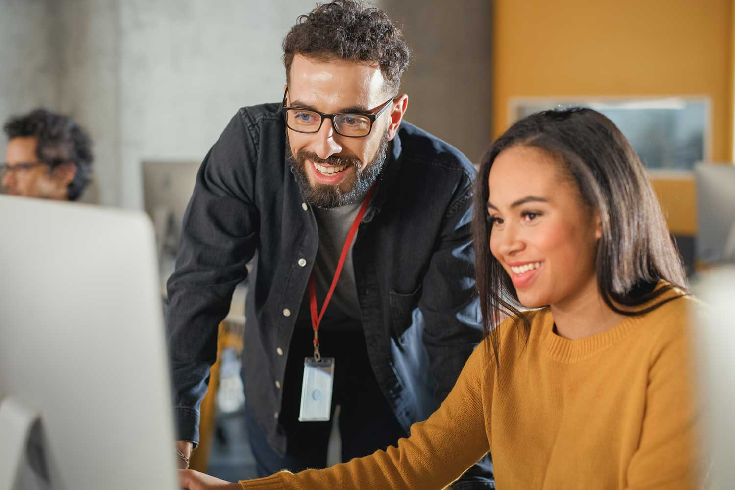 A tutor leans over a desk to look at a student's work on a computer
