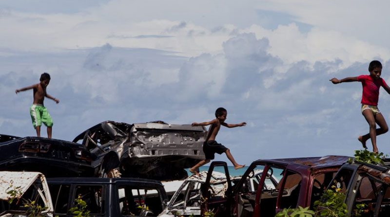 Children jumping over wrecked cars in tropical seas