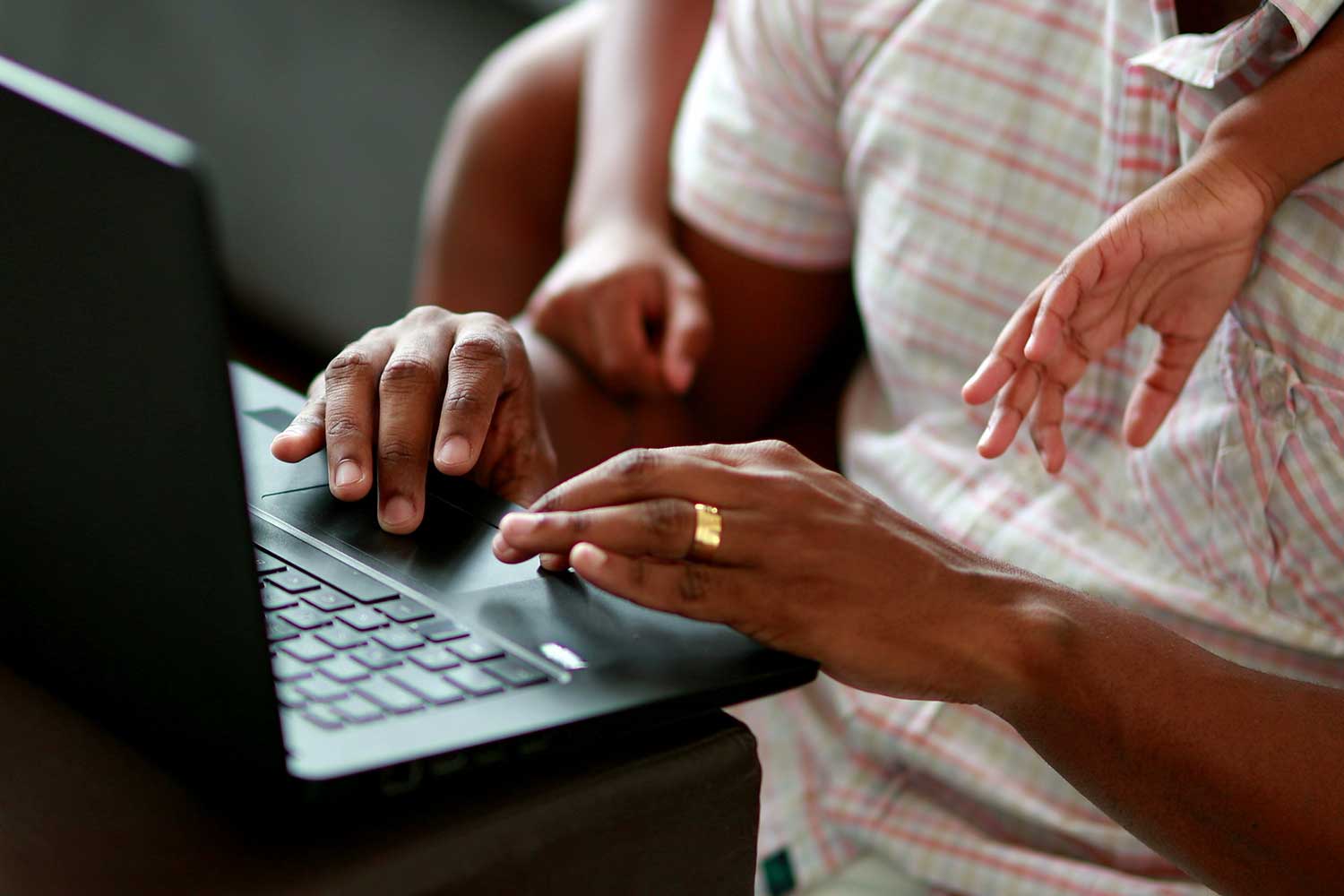 A person types on a laptop while a child leans over them