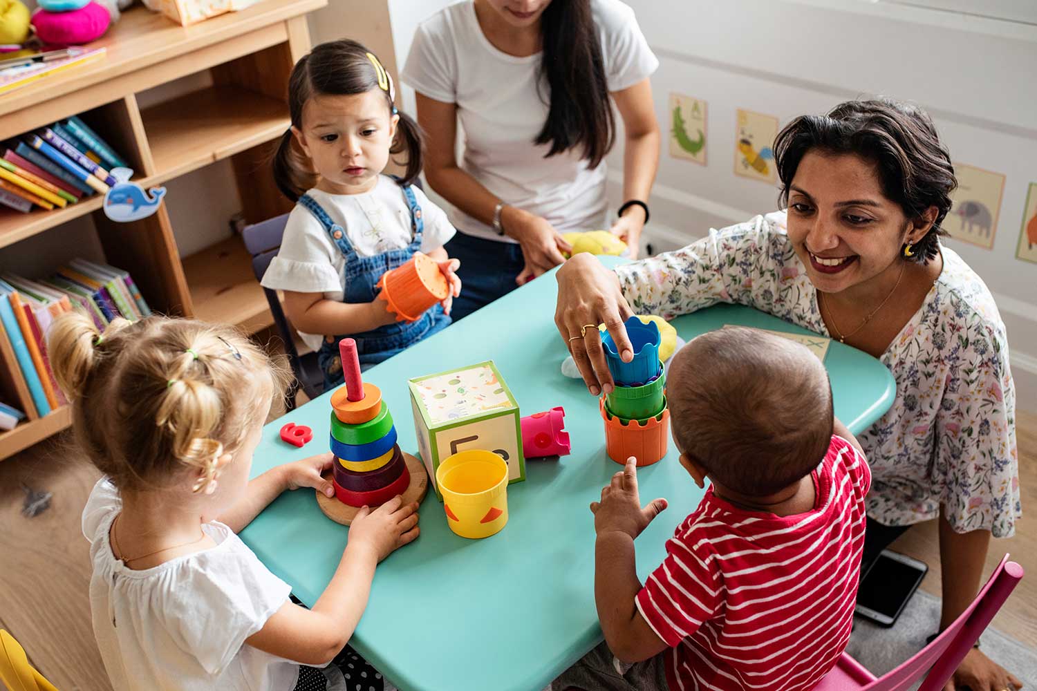A nursery practitioner sits with four young pupils