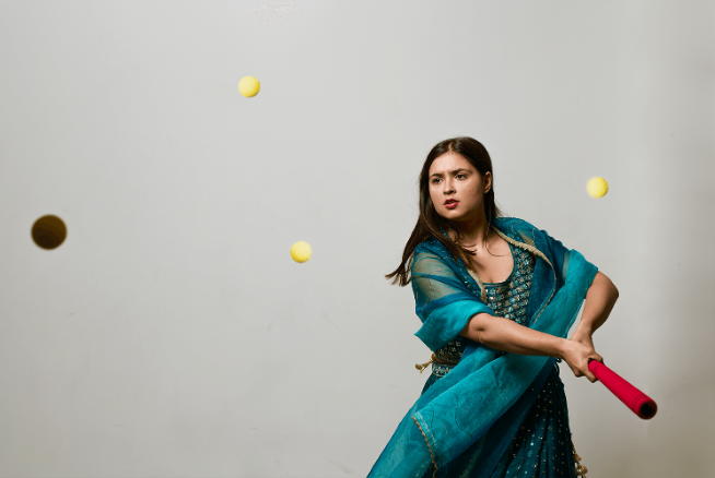 A student stands hitting tennis balls with a bat.