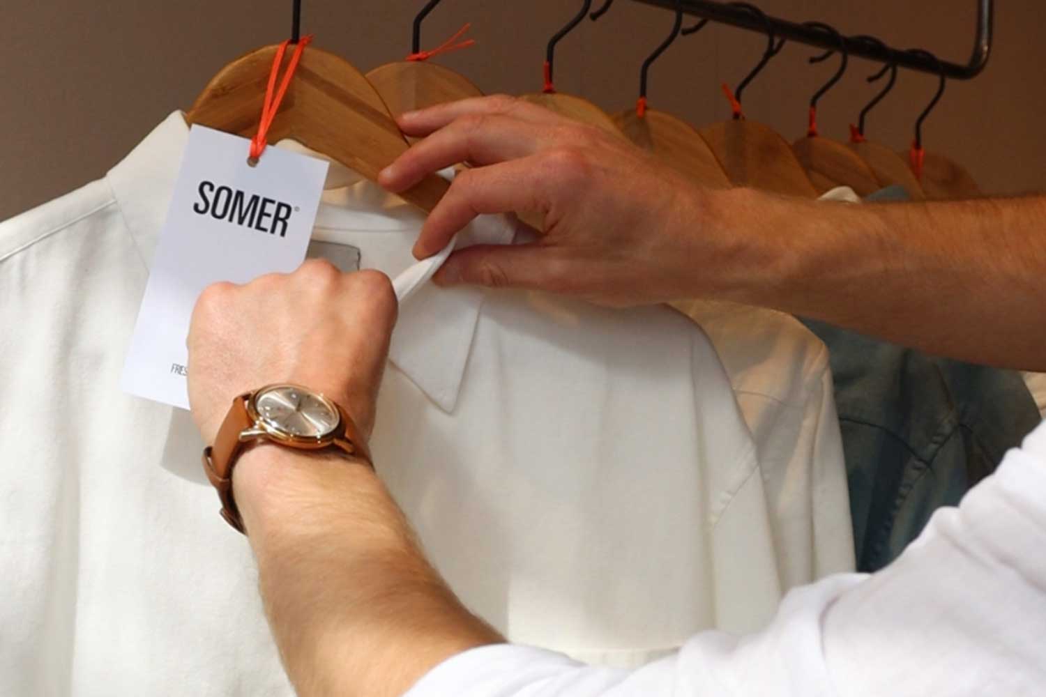 A person straightens the collar of a shirt hanging on a rail