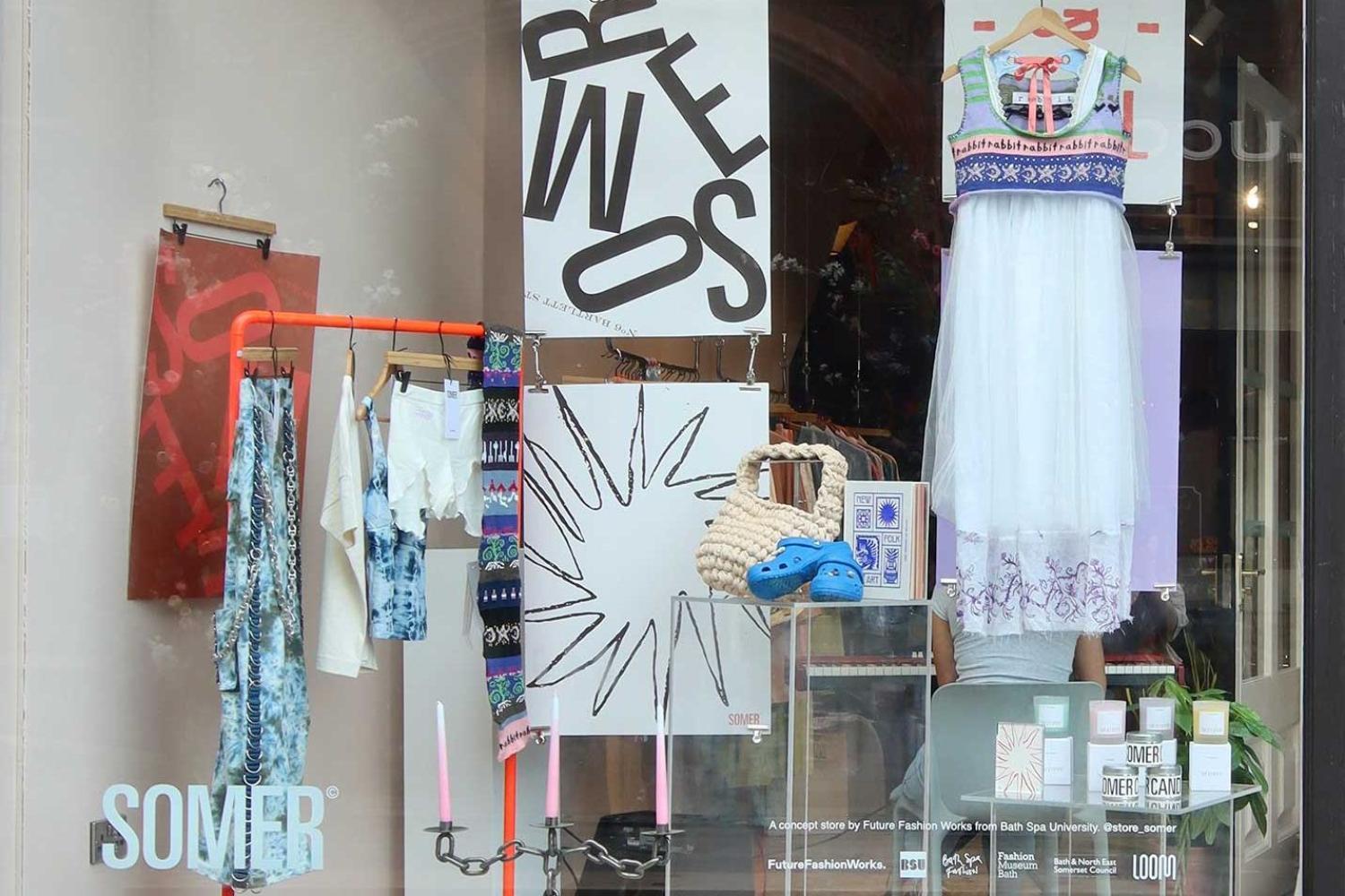 A busy shop window with various textiles and printed posters on display