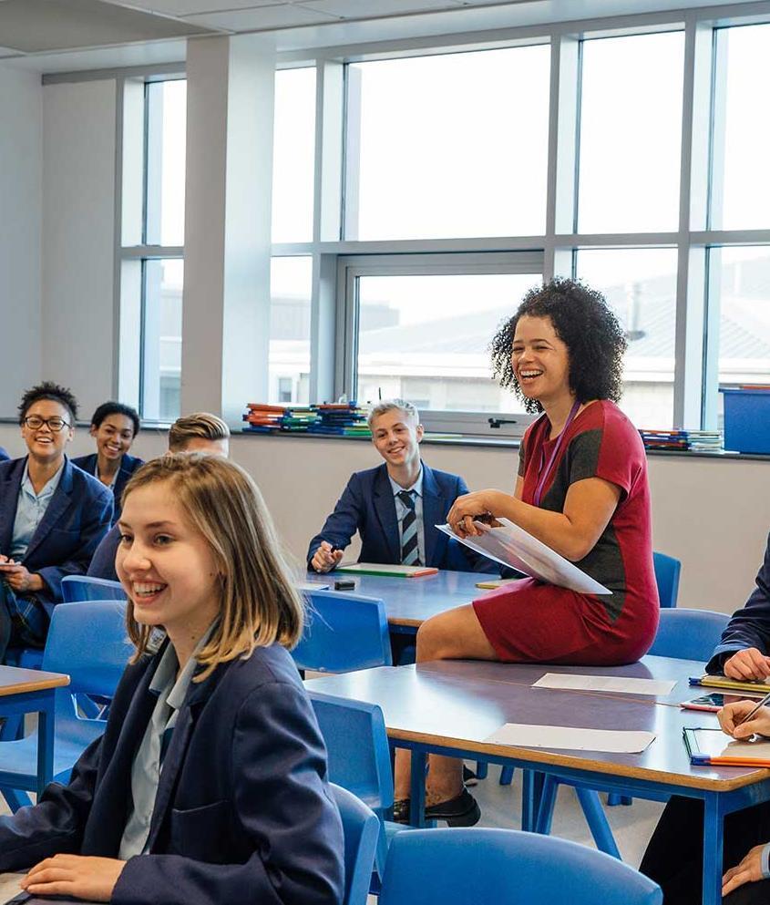 A secondary school teacher sits on a desk during a lesson
