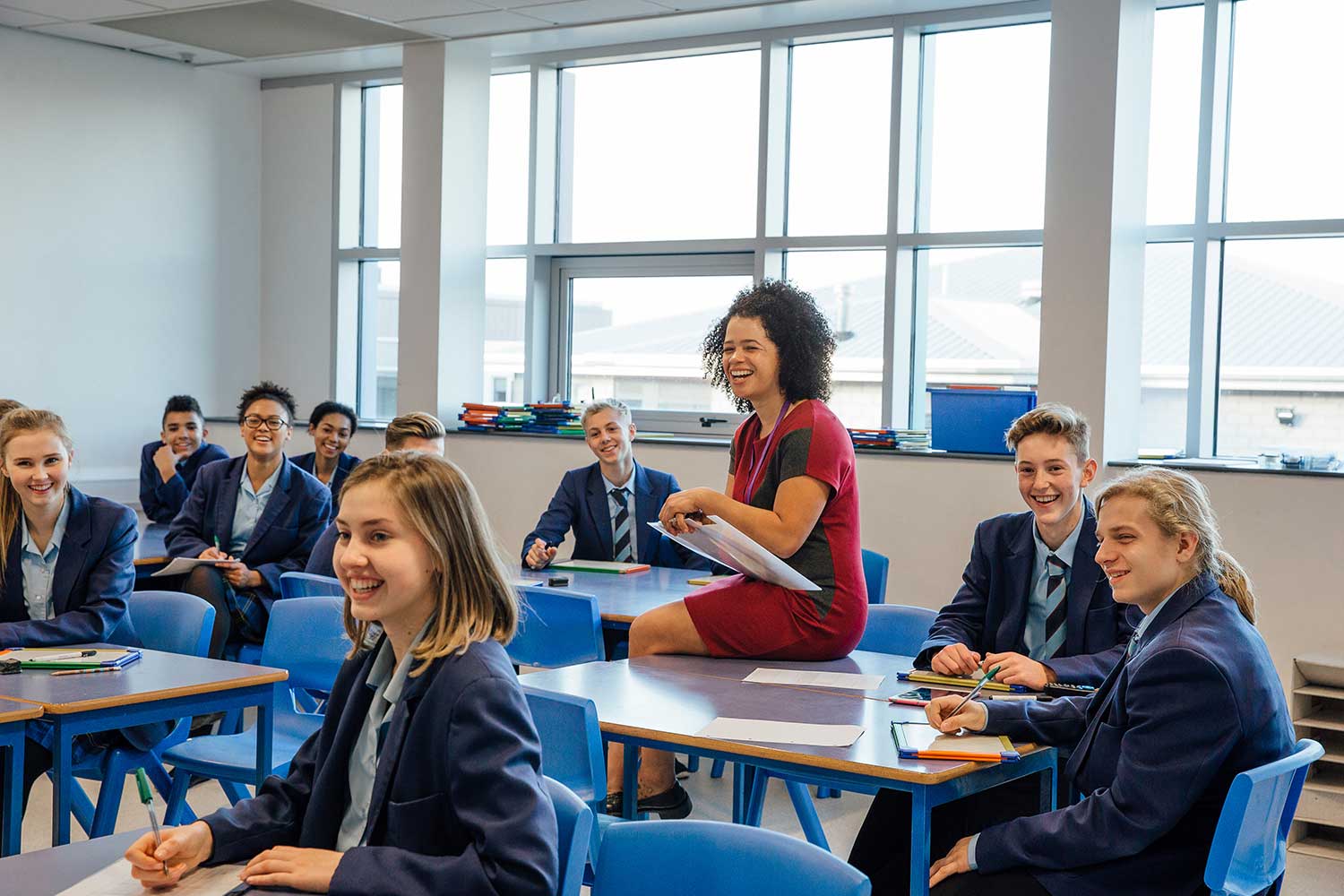 A secondary school teacher sits on a desk during a lesson