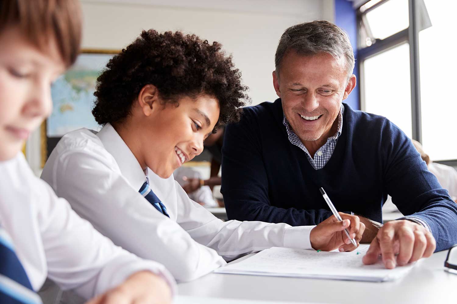 A teaching assistant sits at a desk with a pupil to help them with their schoolwork