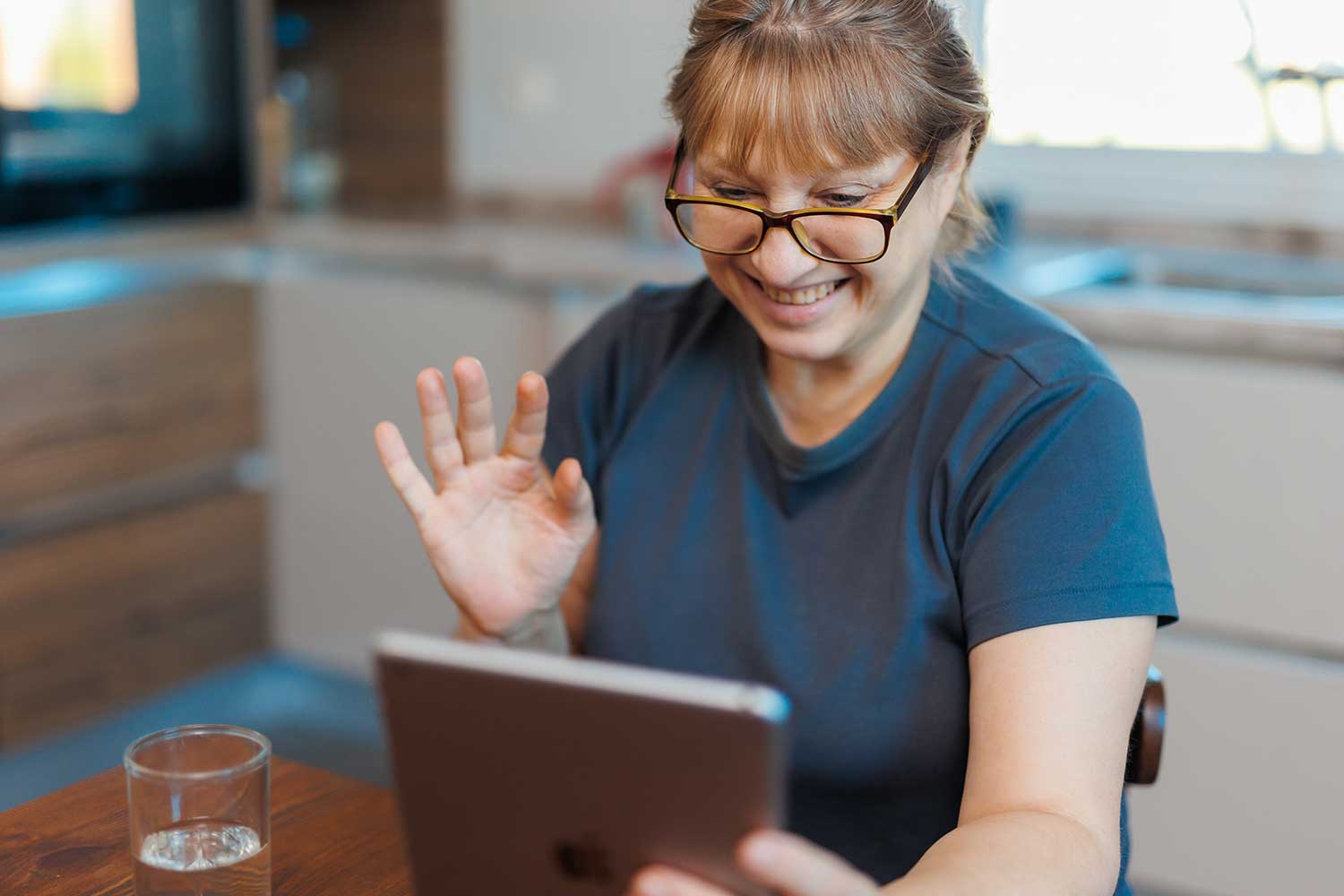 A person sitting in a kitchen takes an informal video call on their iPad