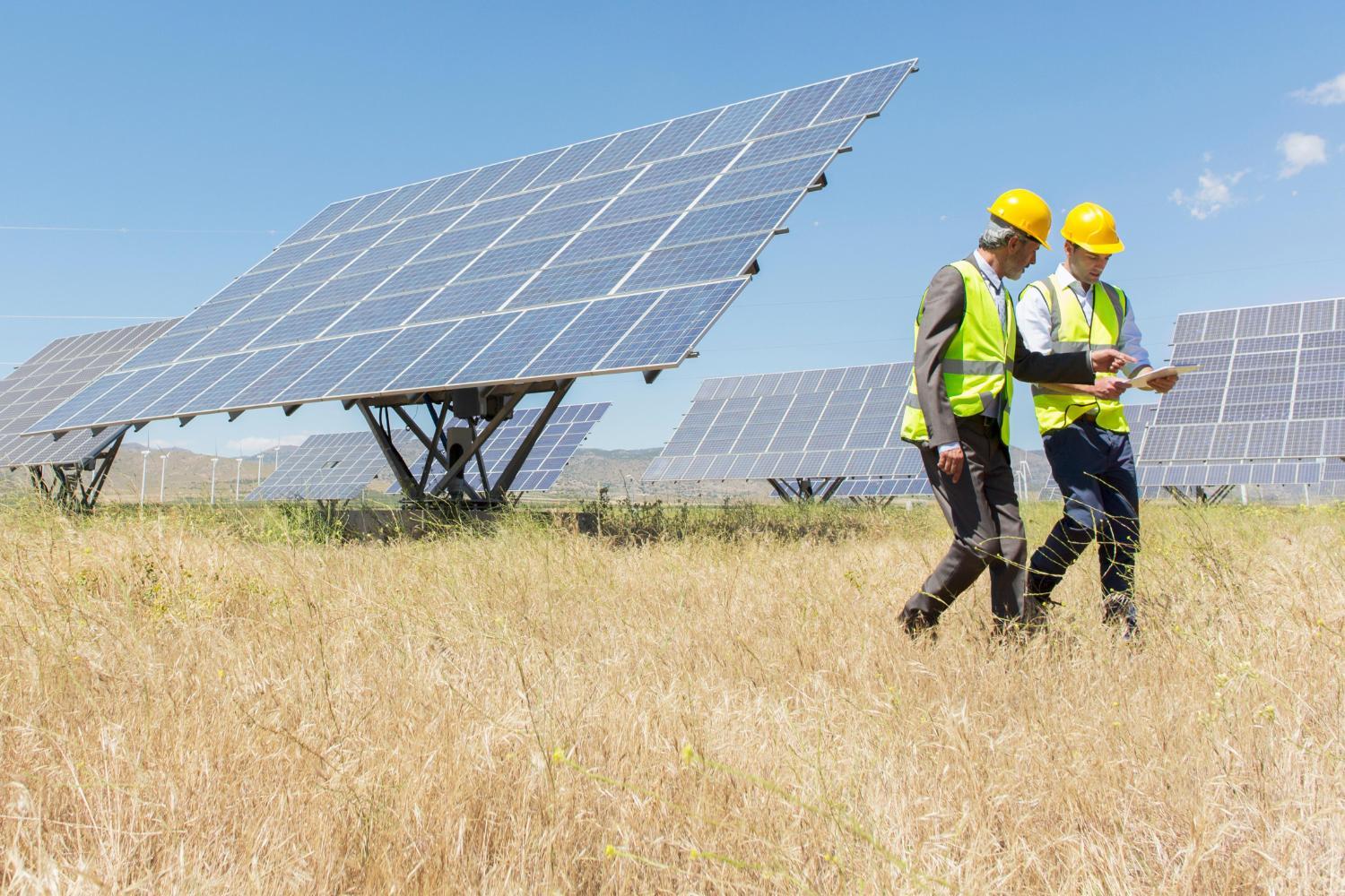 Two workers examine huge solar panels.
