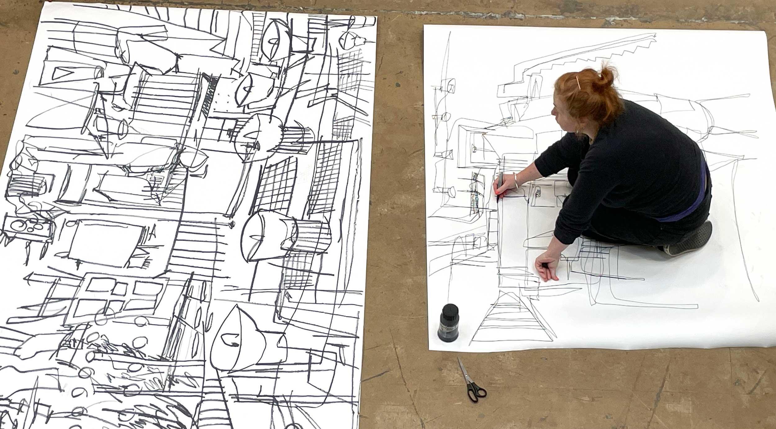 A person kneels on the floor to draw on a large piece of paper