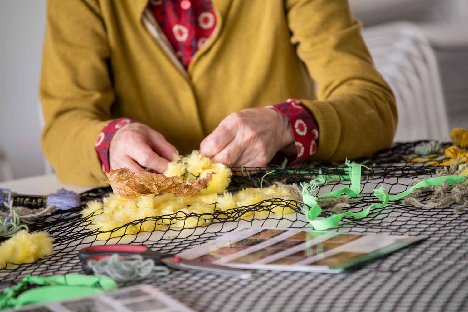 Person in yellow cardigan crafting at a table