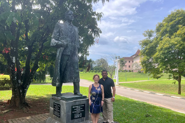 Two people standing underneath a statue of Sir William Ivor Jennings