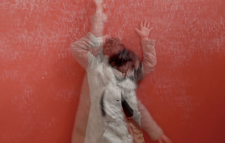 A woman stands in a coat against a red background, blurred in a double exposure