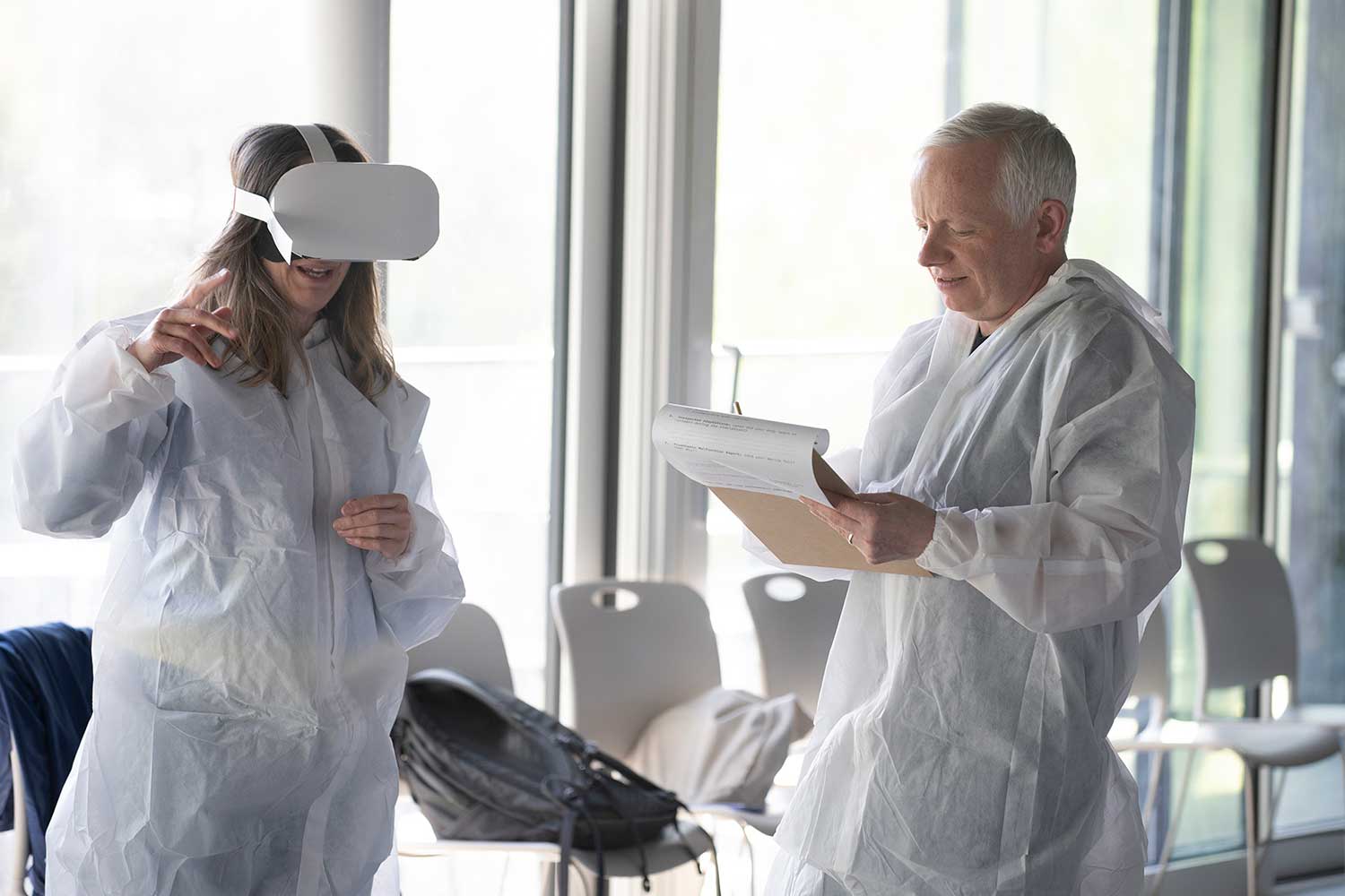 Two people in forensic suits conduct a task involving a VR headset