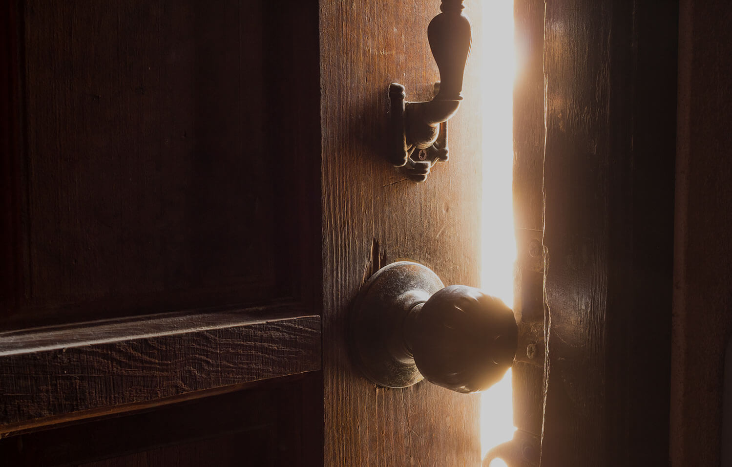 An old, worn wooden door is left slightly ajar, with sunlight streaming through