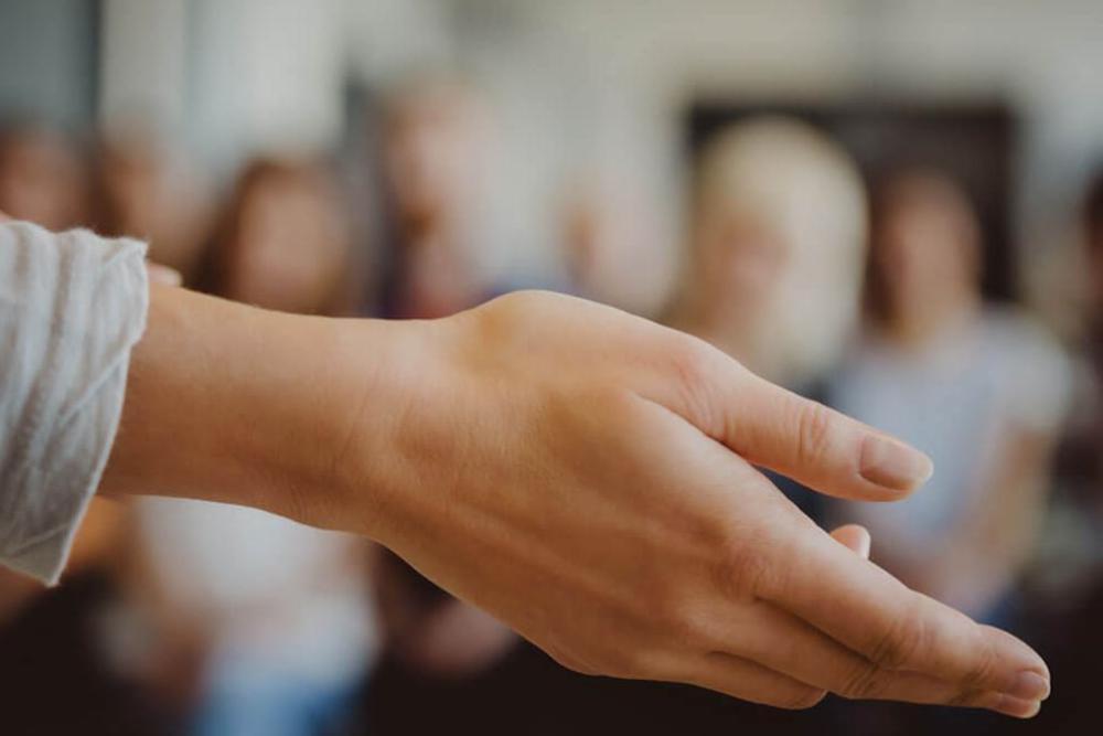 abstract photo of a hand gesturing in front of an out of focus audience