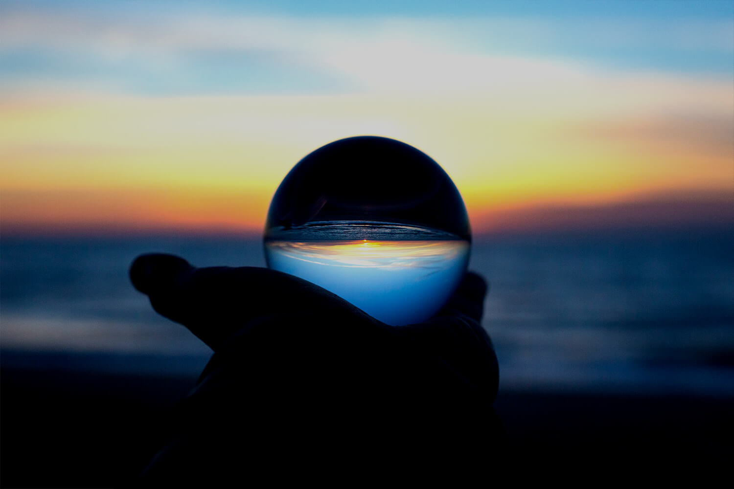 Person holding a glass ball in front of a sunset