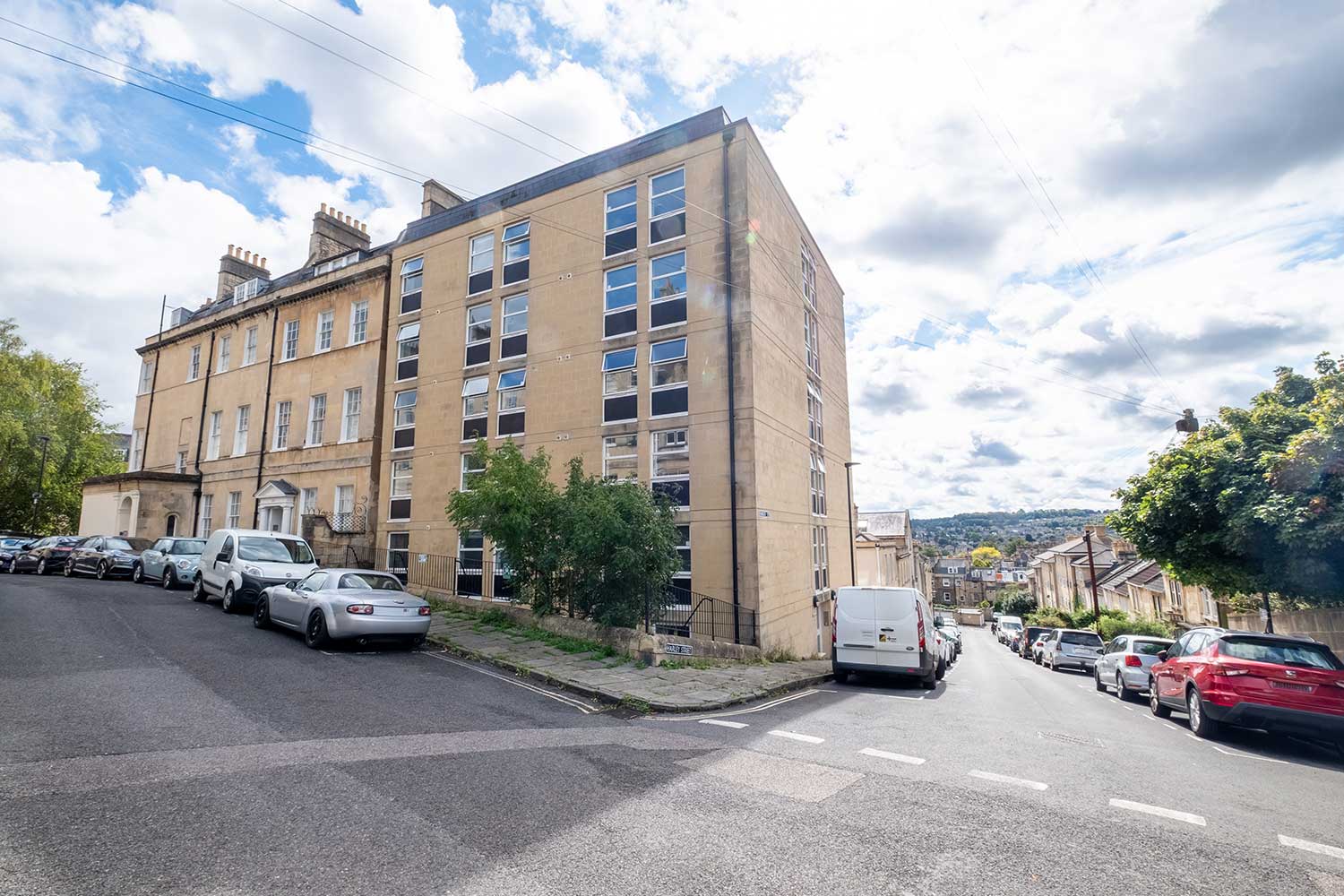 A building with several floors on the corner of a street lined with cars