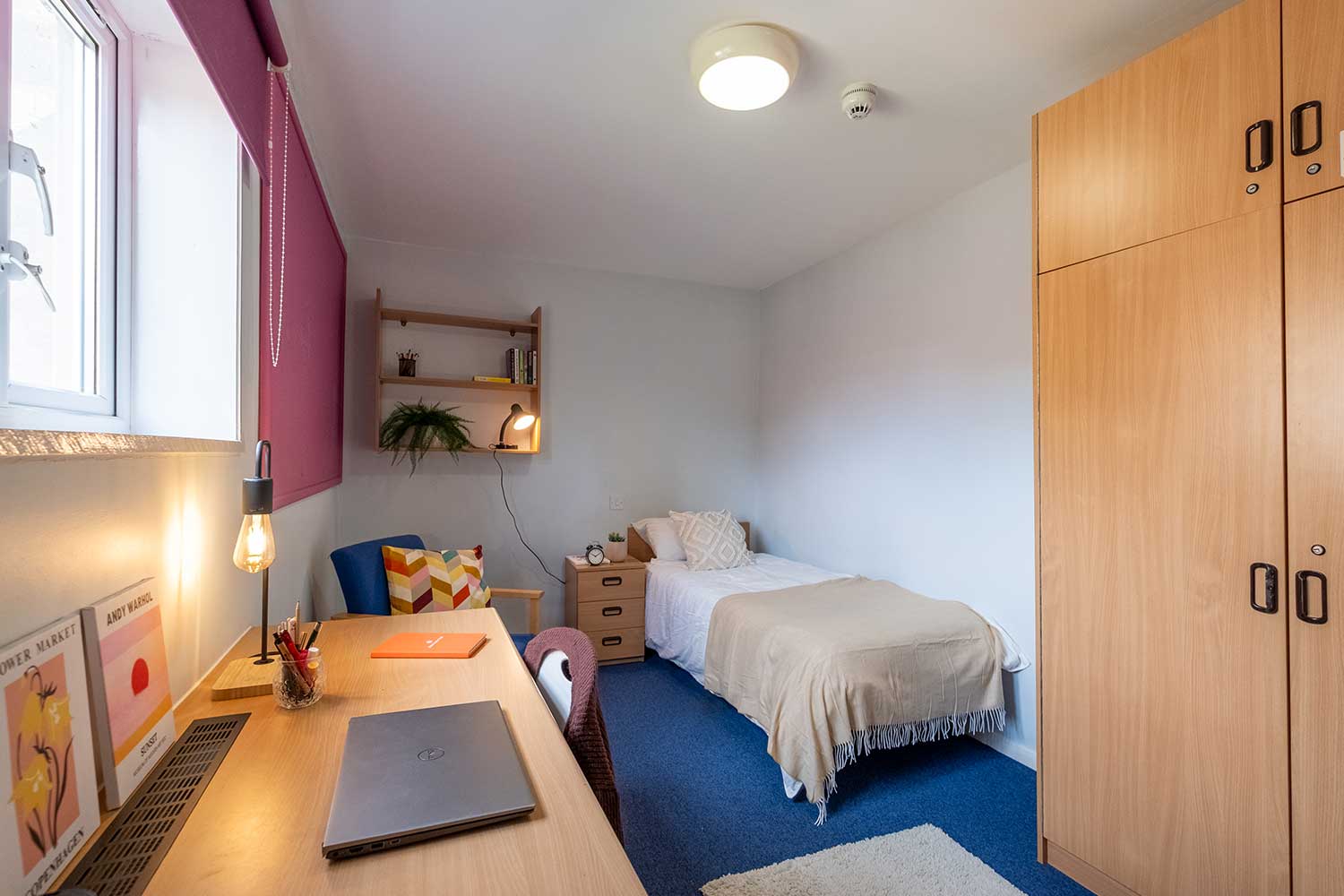 A student bedroom with a bed, desk, wardrobe and chair