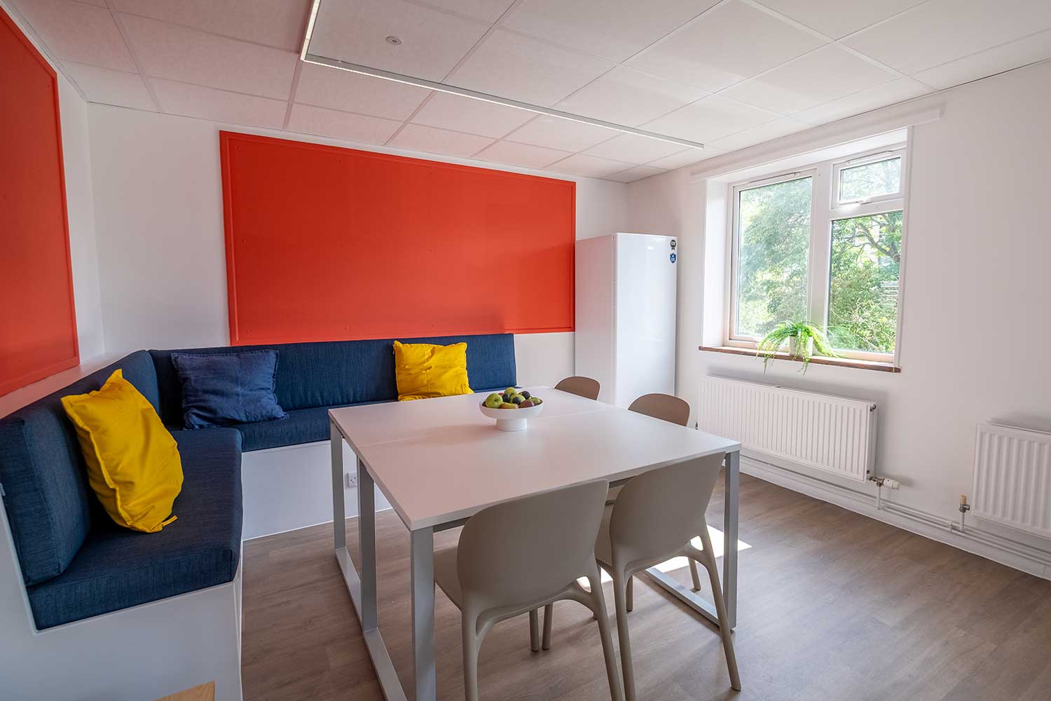 A colourful seating area with a table, chairs and bench situated near a window