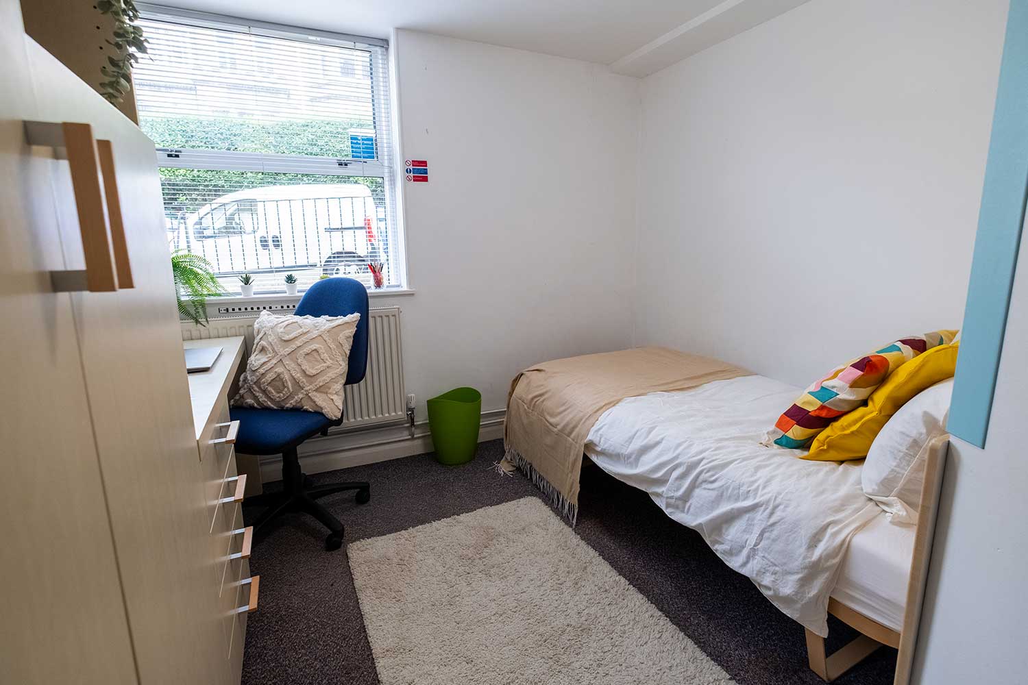A student bedroom with a bed, desk, wardrobe and window