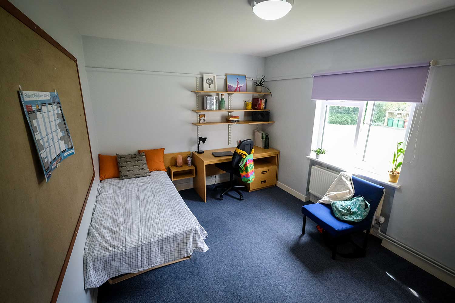 A large bedroom with a bed, desk, chair and noticeboard