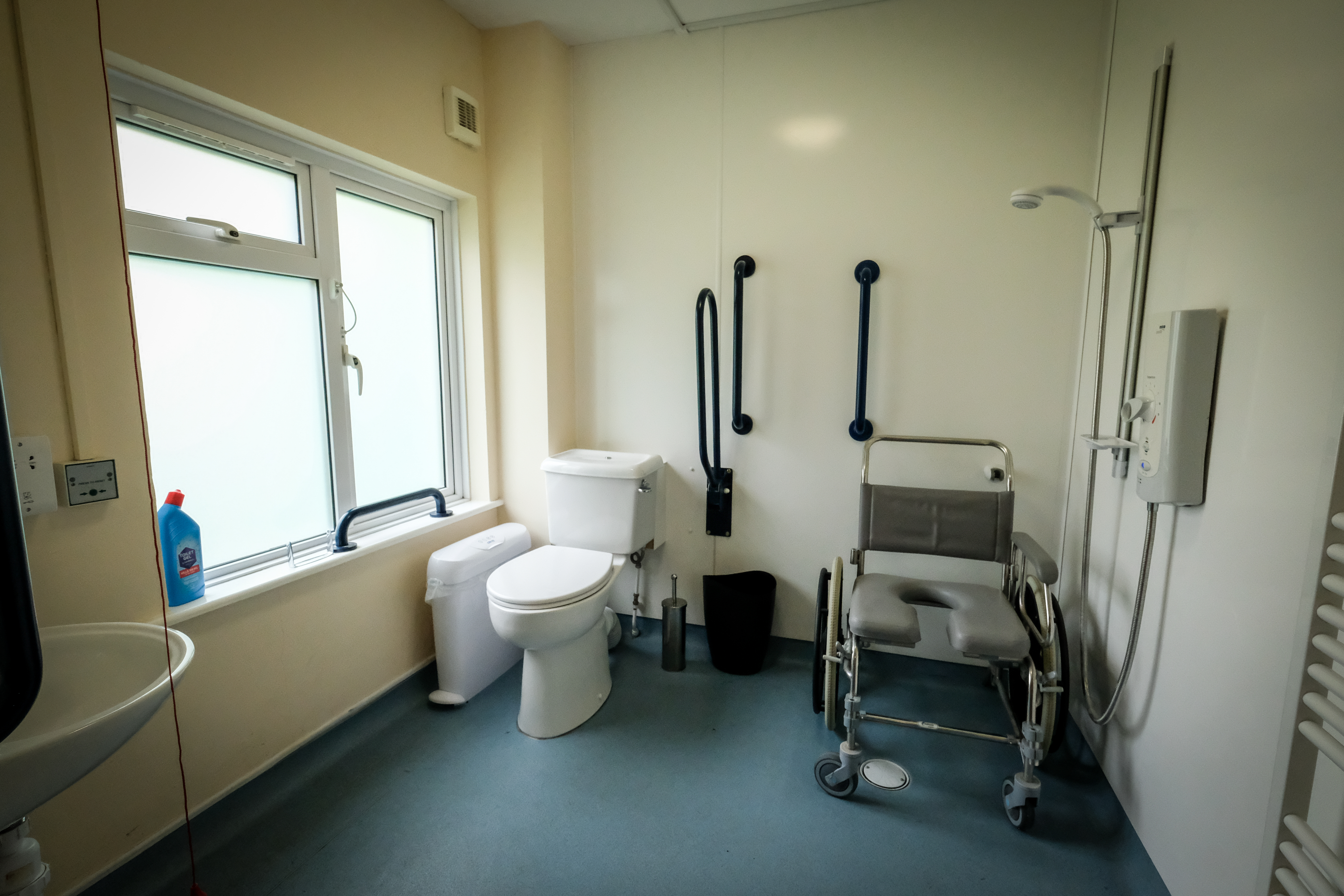 A large bathroom with additional handrails, a walk-in shower on a level surface and a wheeled chair suitable for use in the shower