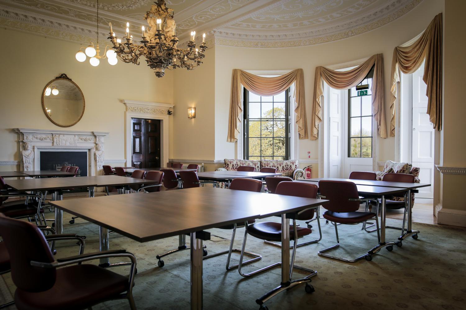A large room with Georgian period features, large sash windows, chandelier and several tables and chairs set up as desks