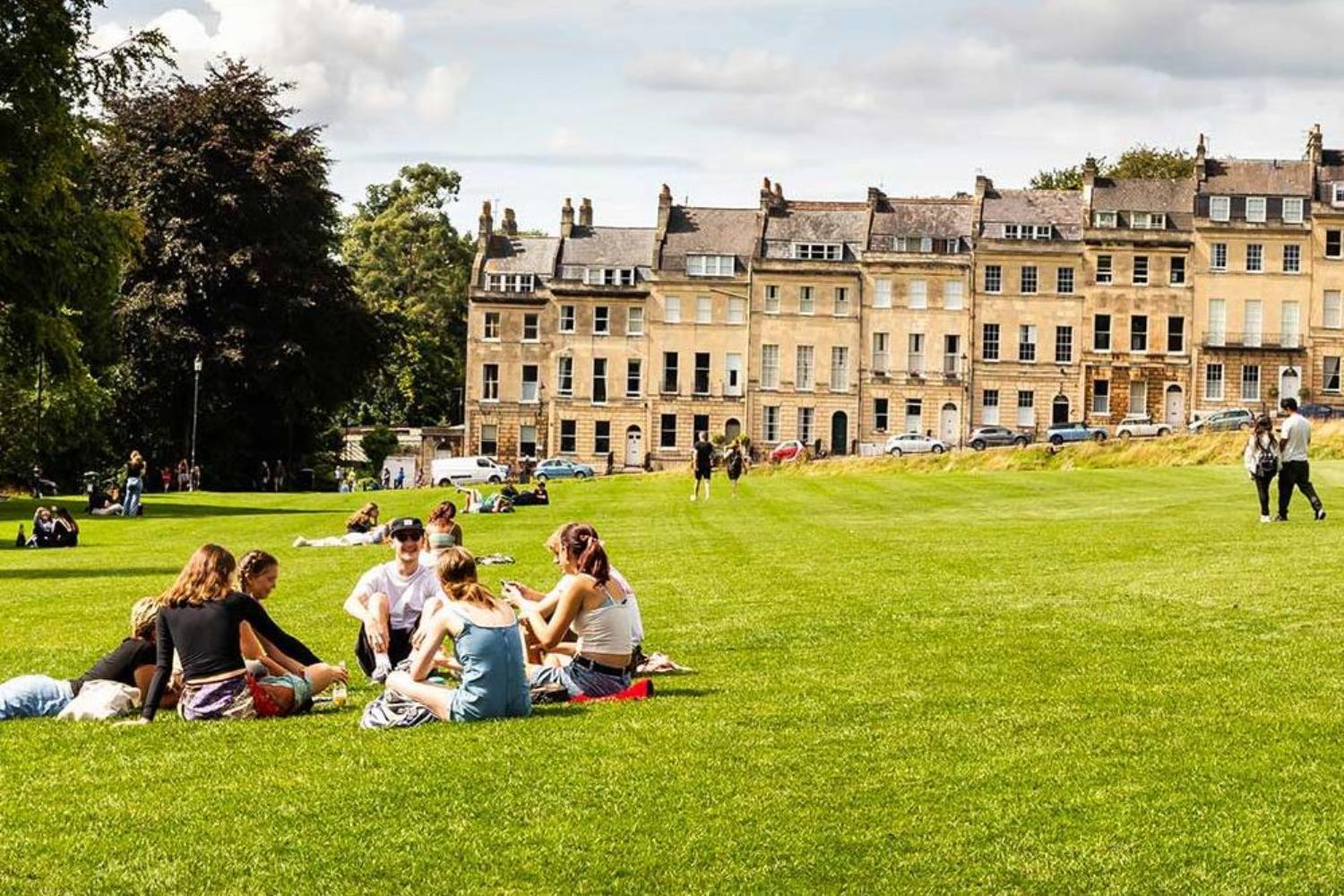 Young people sitting in groups on the green in front of Georgian Royal Crescent Bath