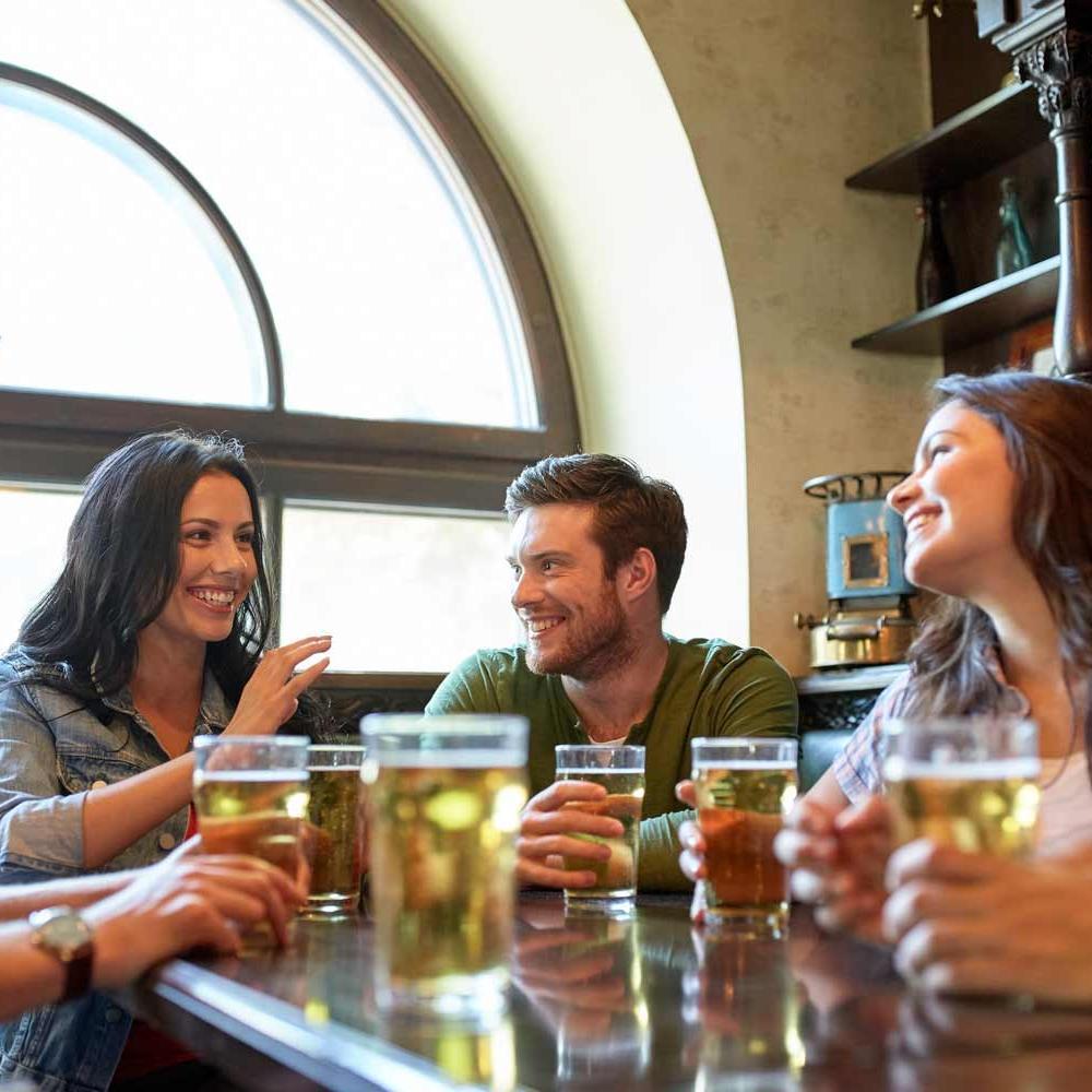 Group of young people sitting around a table with pints of beer laughing