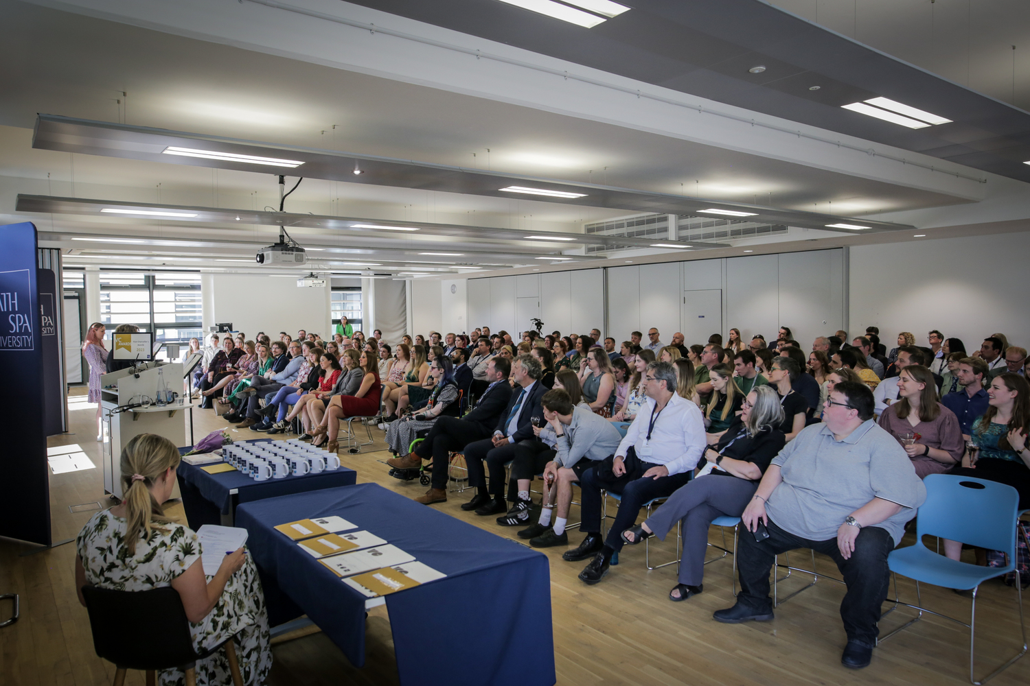 A lecture hall with an audience full of people looking at the speaker