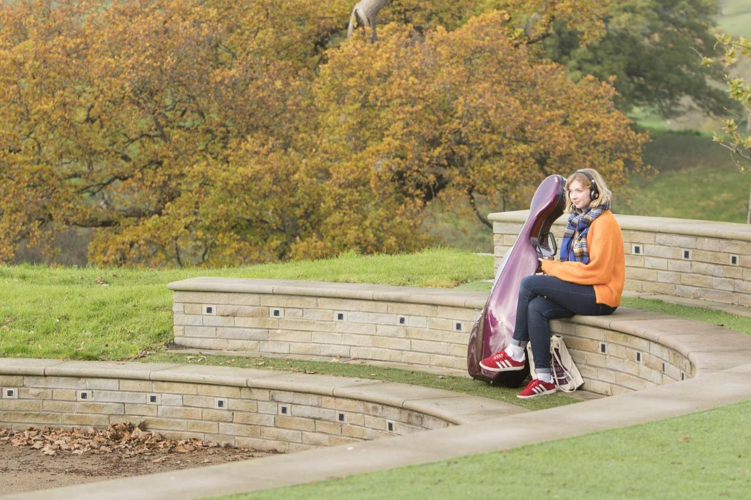 A student sits at an empty amphitheatre in a scenic location surrounded by greenery and trees