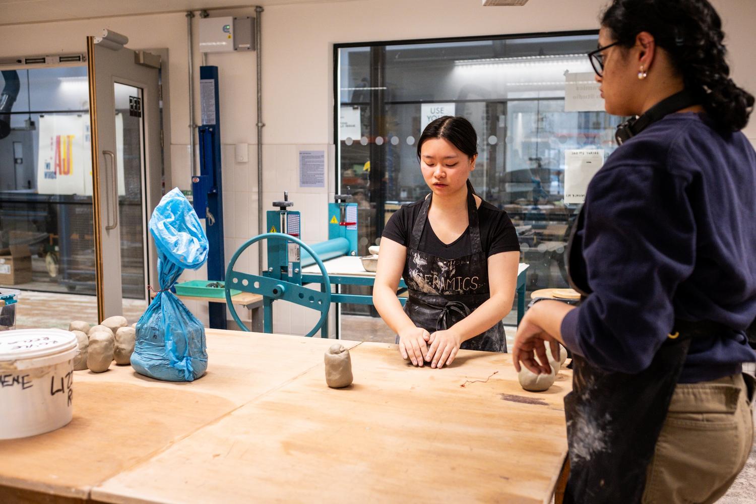 Two students stand at a large table in a pottery studio