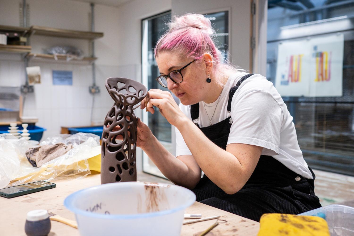 A person with pink hair leans over an intricate sculpture