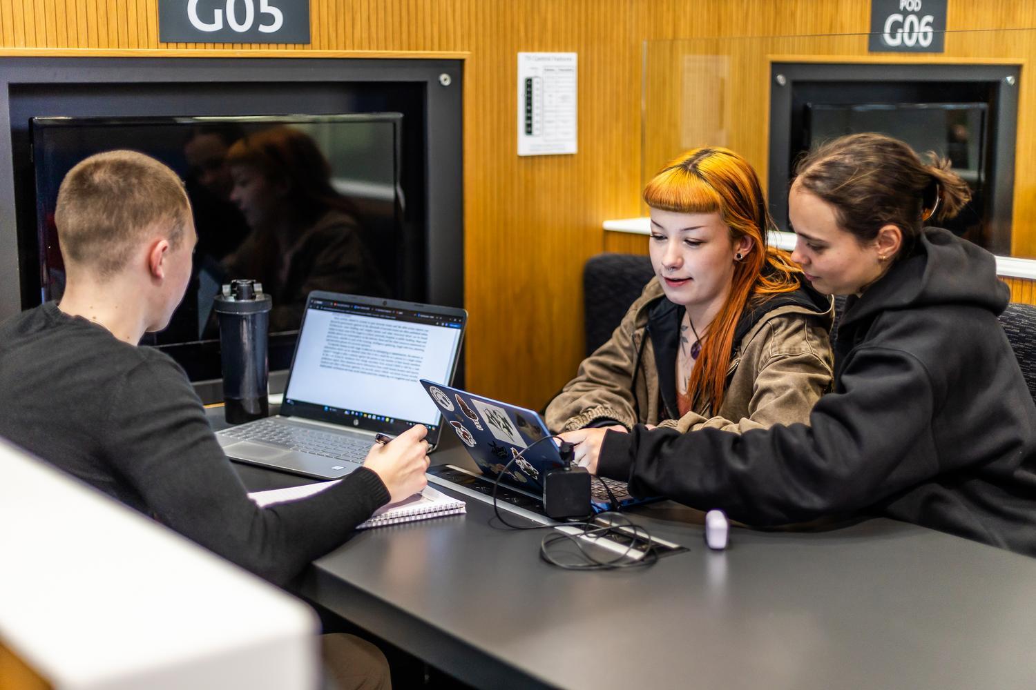 Three students sit in a booth while looking at their laptops