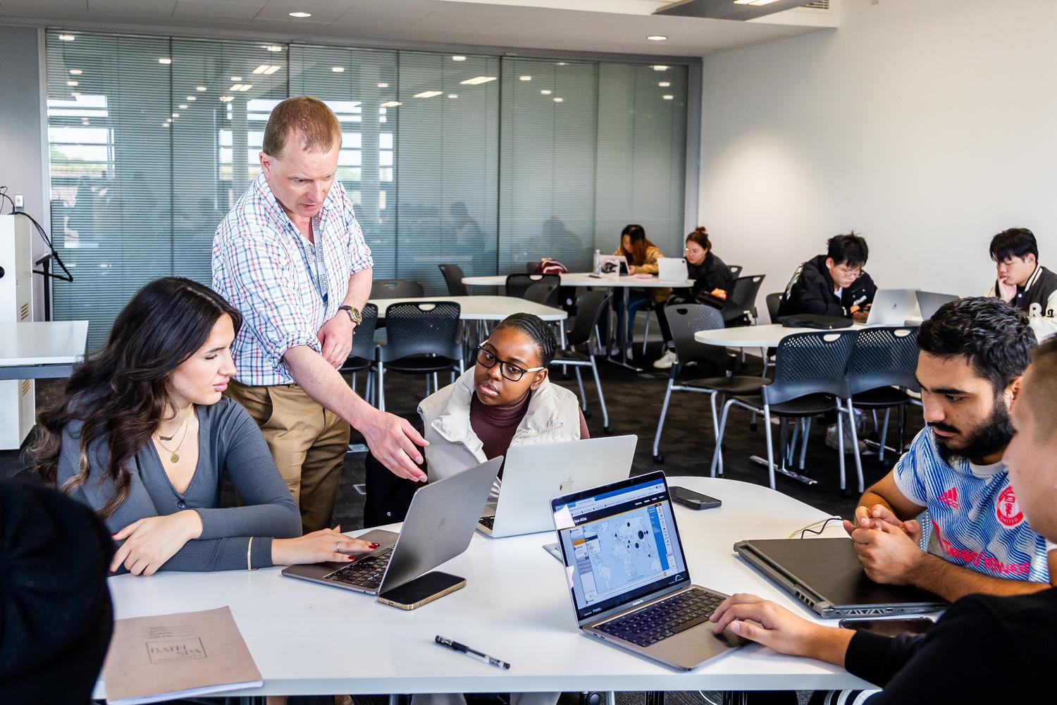 A seminar with students sitting at tables and a lecturer speaking to one person