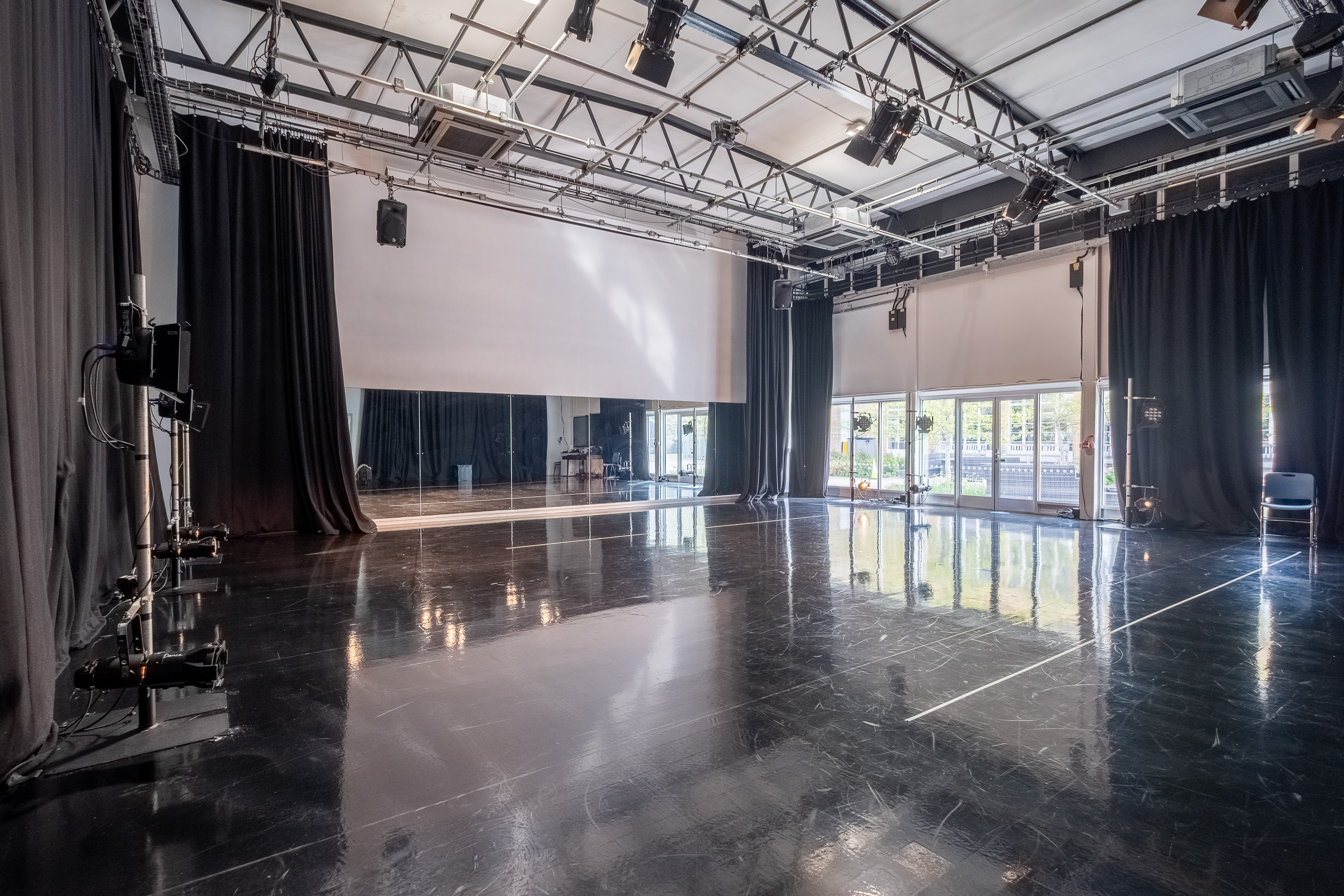 A large, empty dance studio with black flooring and curtains, lighting rig and large mirrors