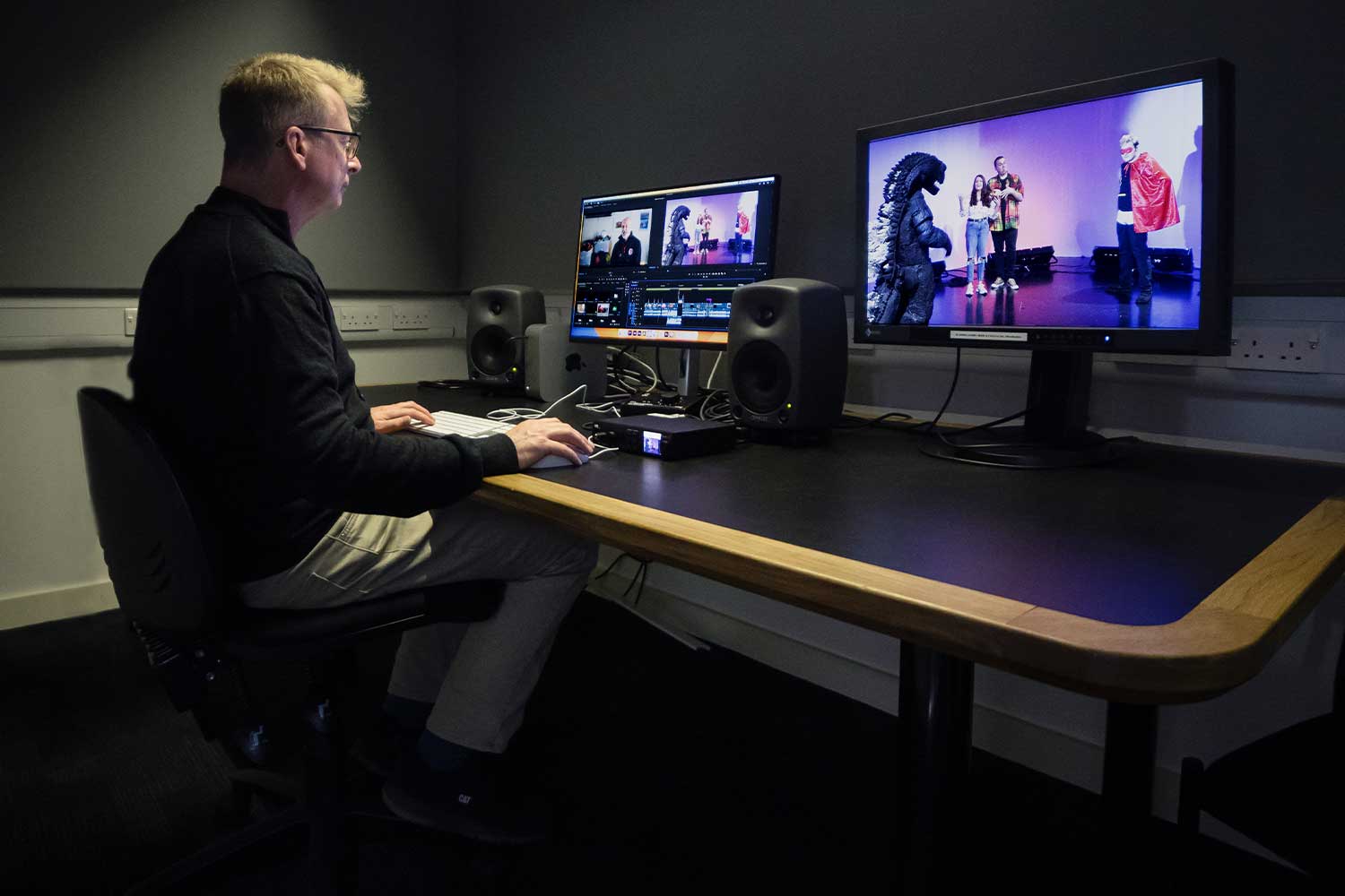 A person sits at a desk with screens showing them editing video content