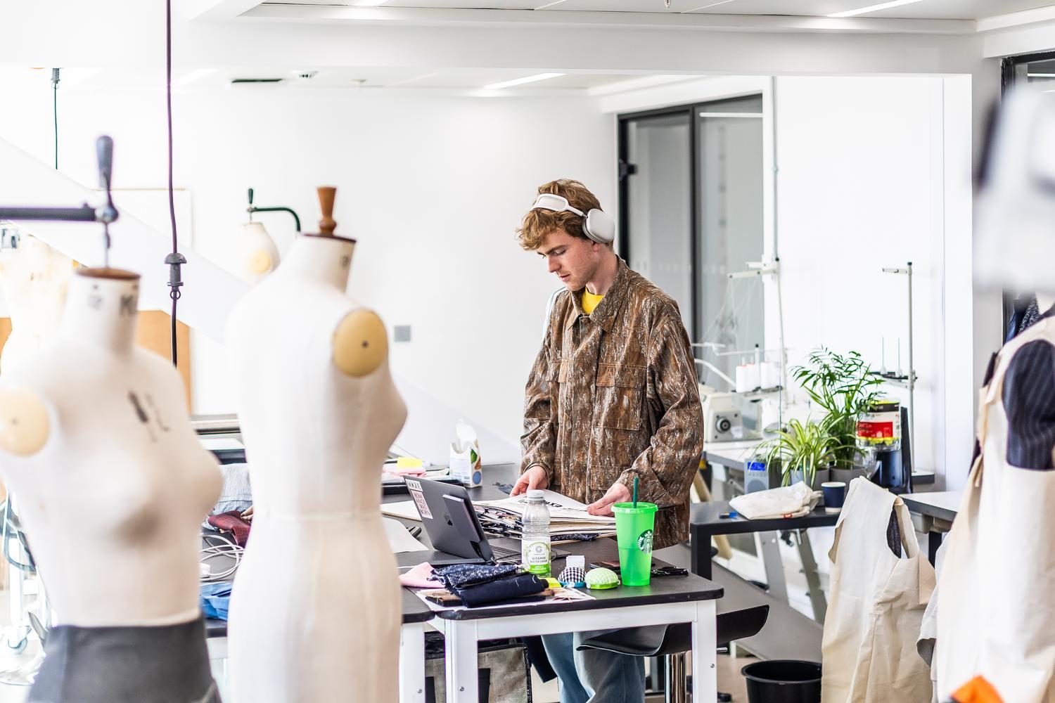 A student leans over their sketchbook and is surrounded by mannequins
