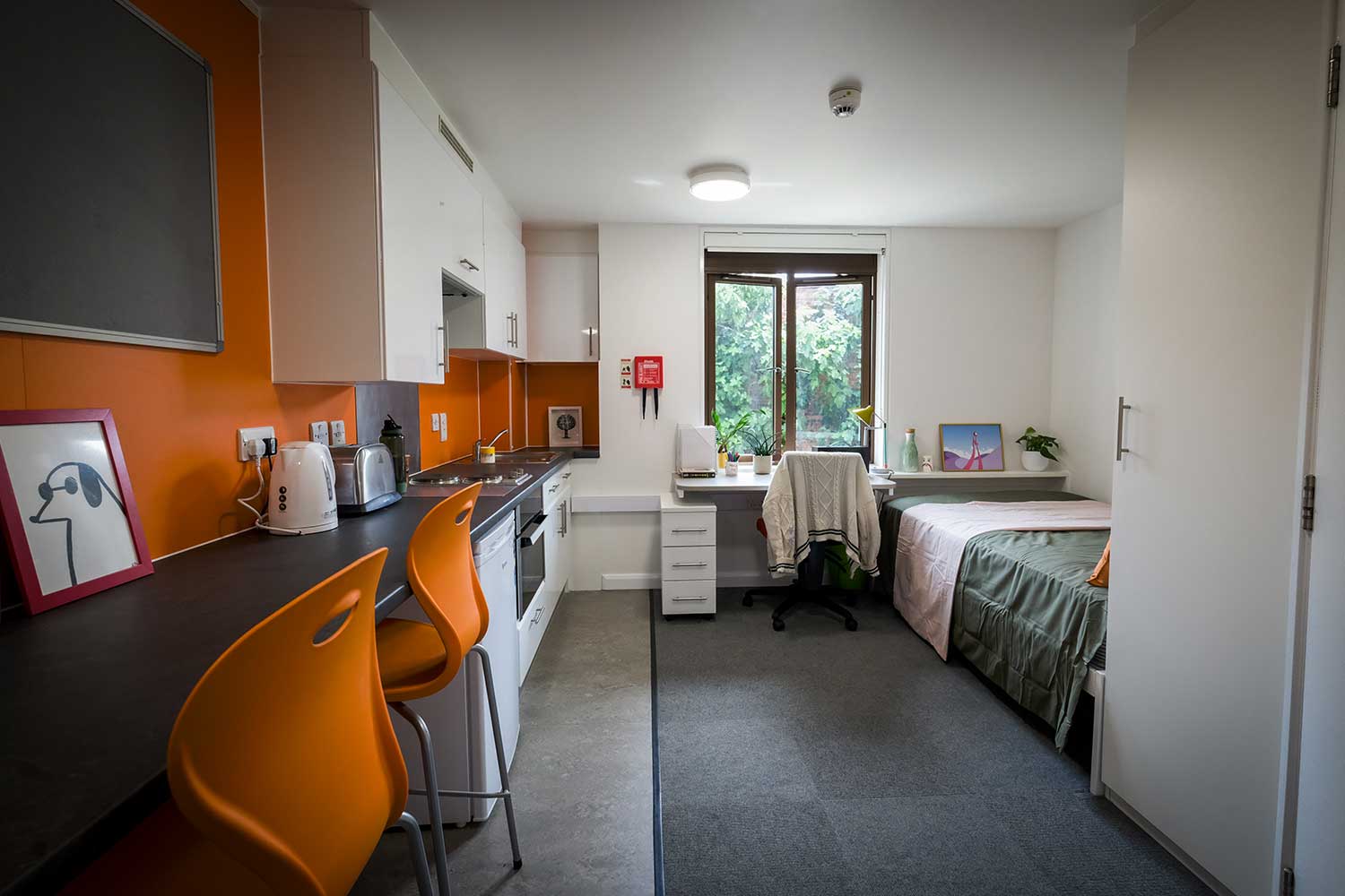 A small studio apartment with colourful orange chairs and accent wall