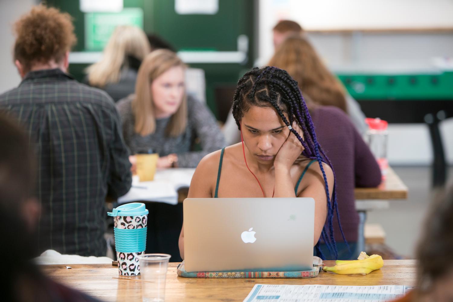 A person leans over a laptop in a shared study space