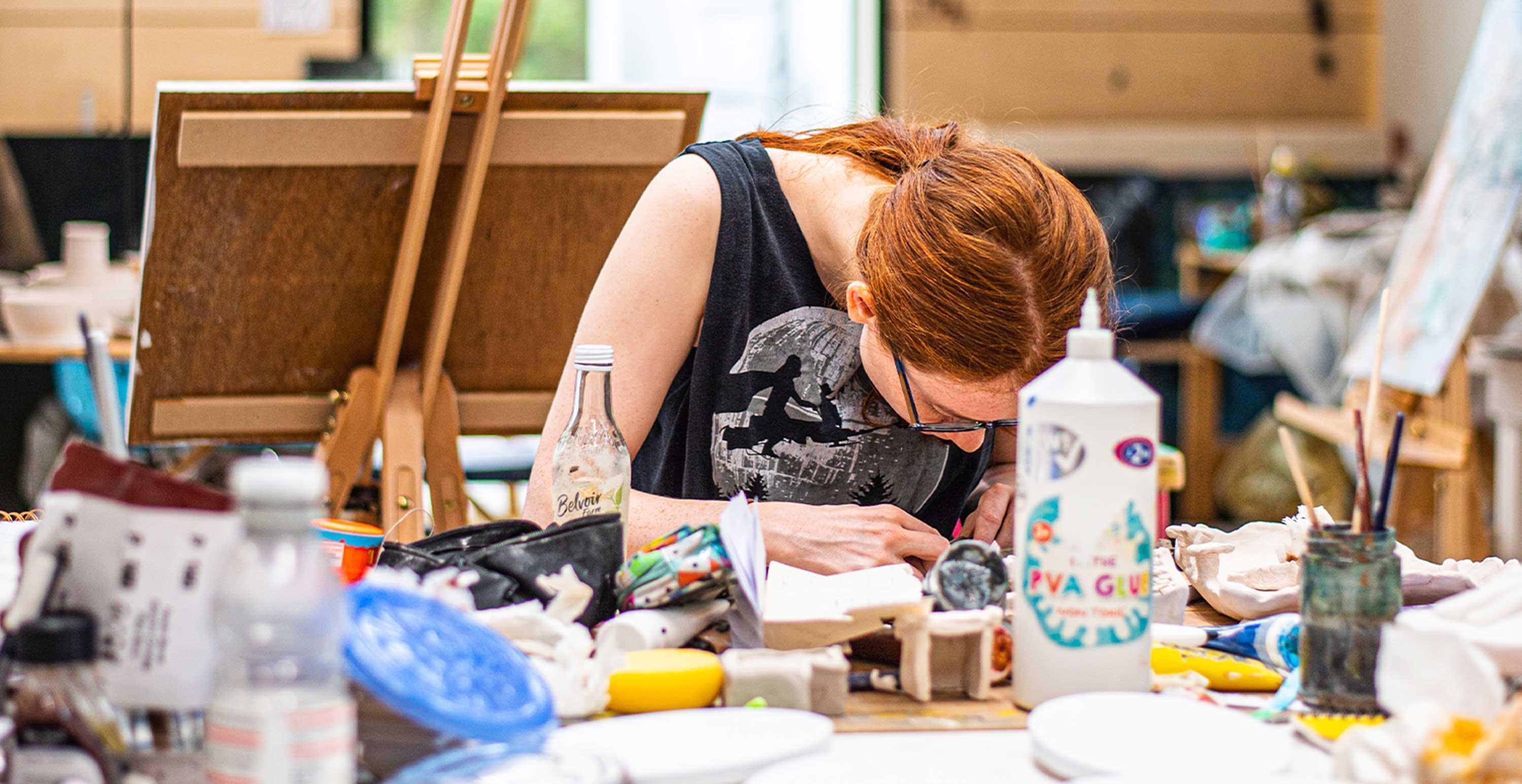 A student leans over a desk as they work on an art project