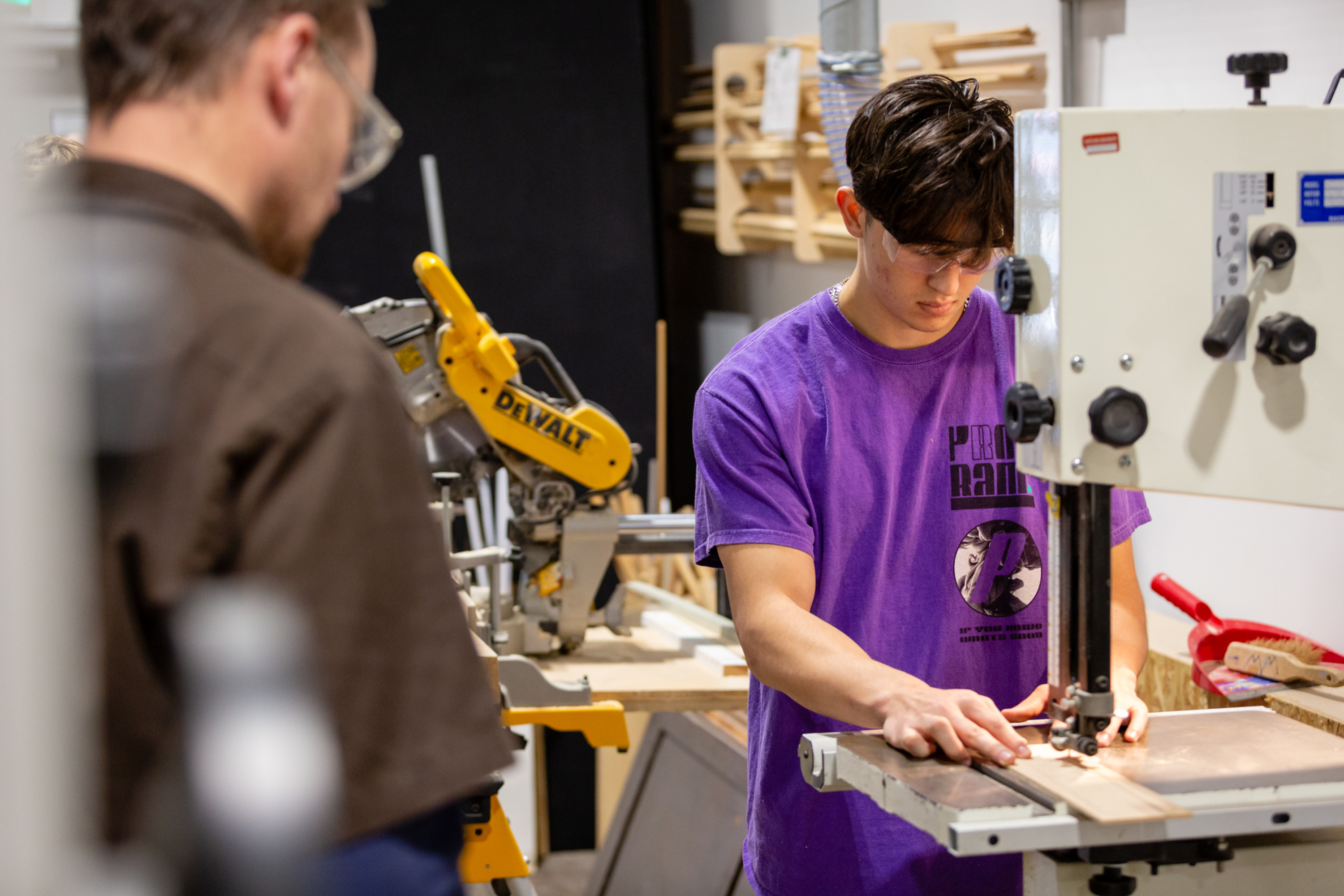 A member of staff supervises a student using woodwork equipment