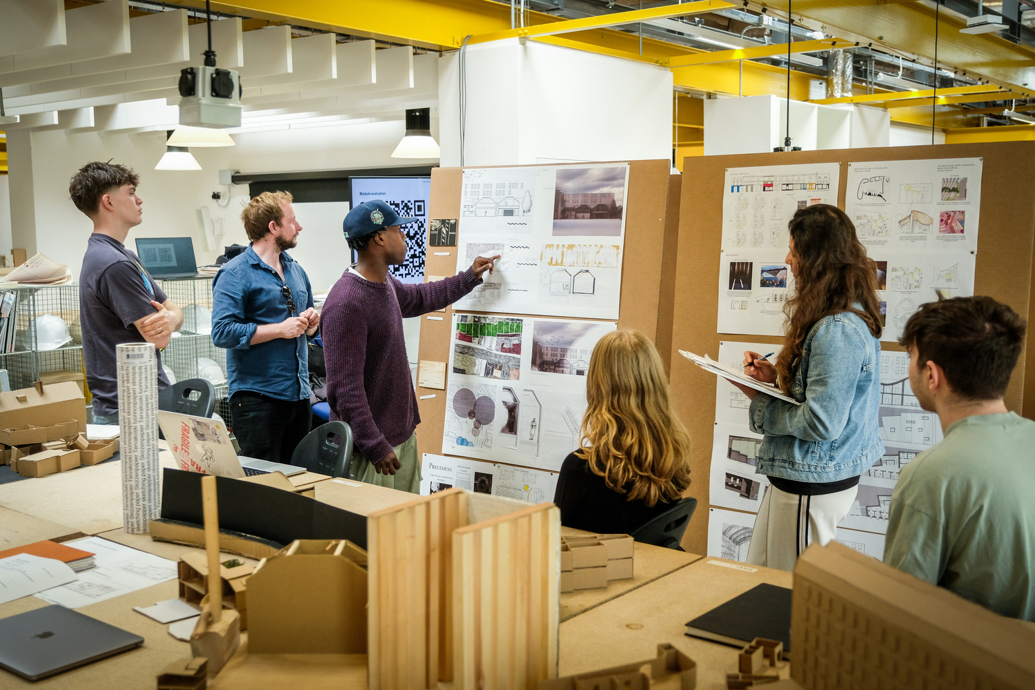 Architecture students share ideas while looking through sketches displayed on a board