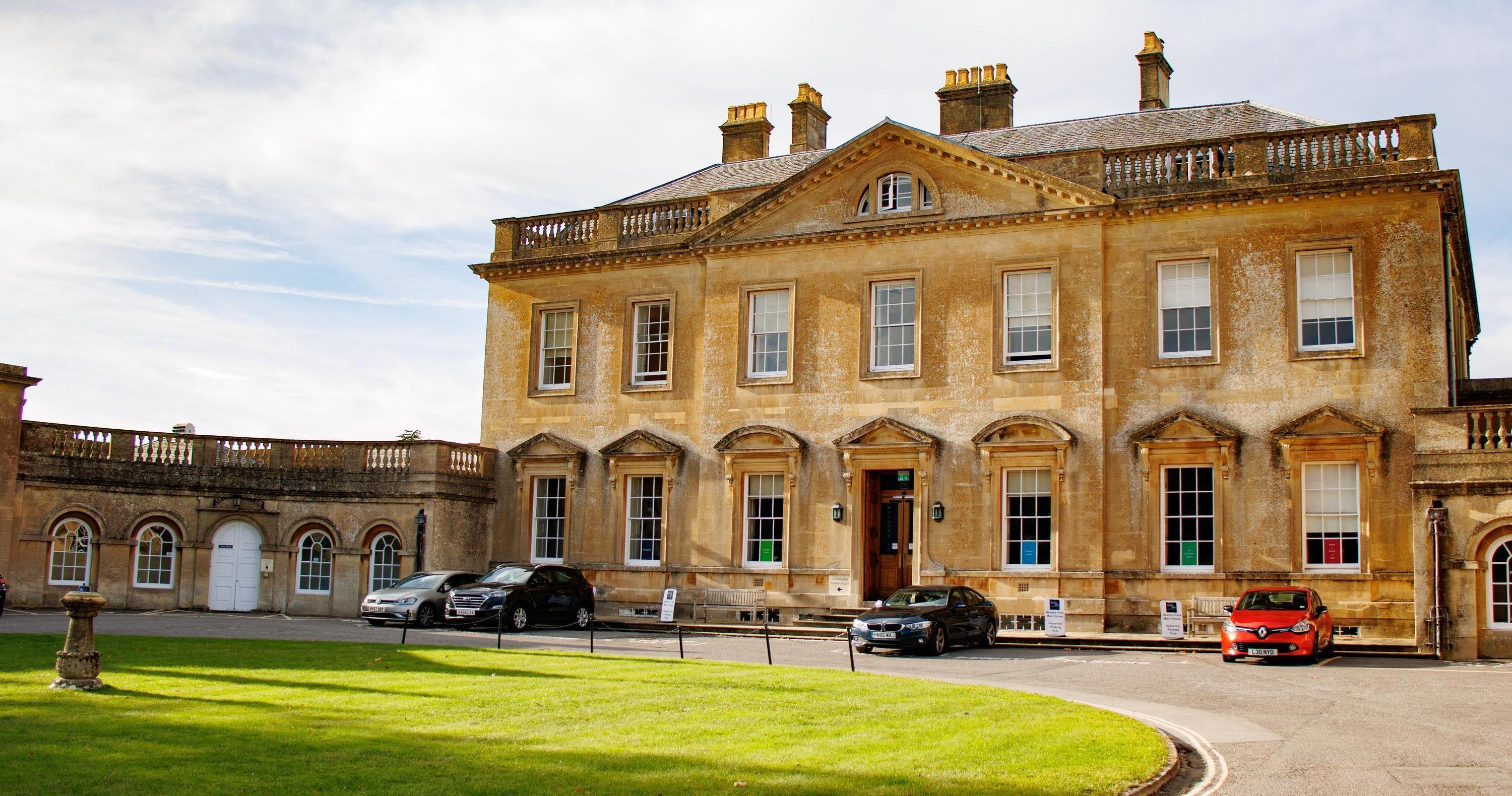 A manor house with three cars parked in front and a large circular lawn
