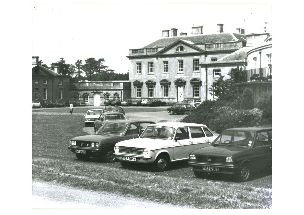 An old black and white photo of a manor house with cars parked on the lawn in front of it
