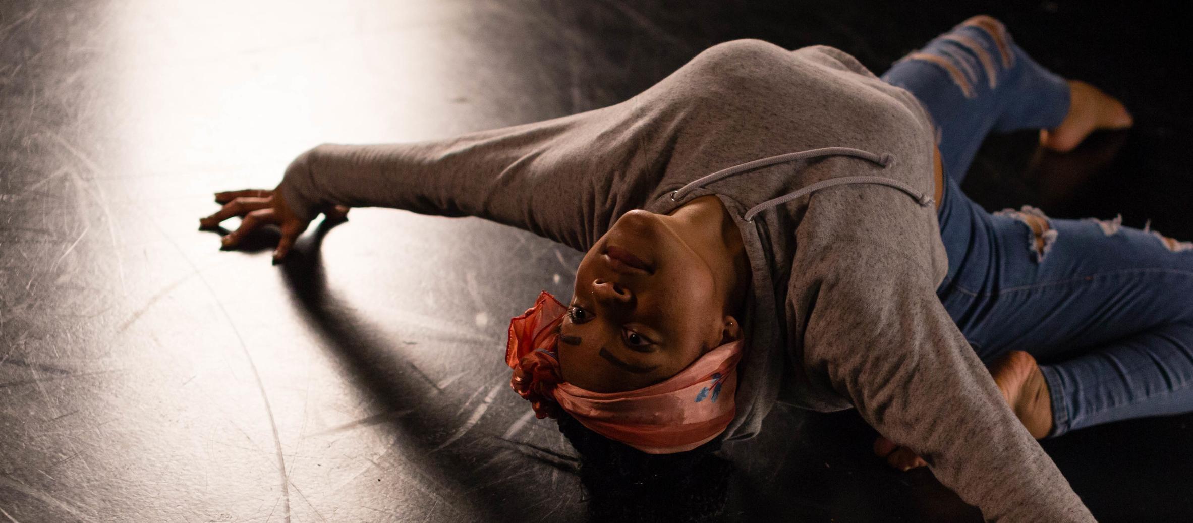 A dancer leans backwards on the floor of a dimly lit stage