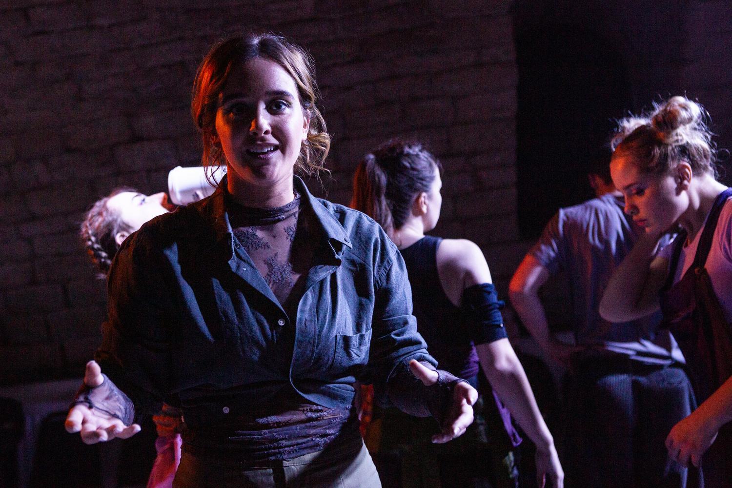 Actors and dancers on stage, with one looking directly at the camera