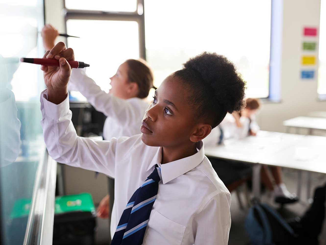 A pupil wearing school uniform writes on a whiteboard