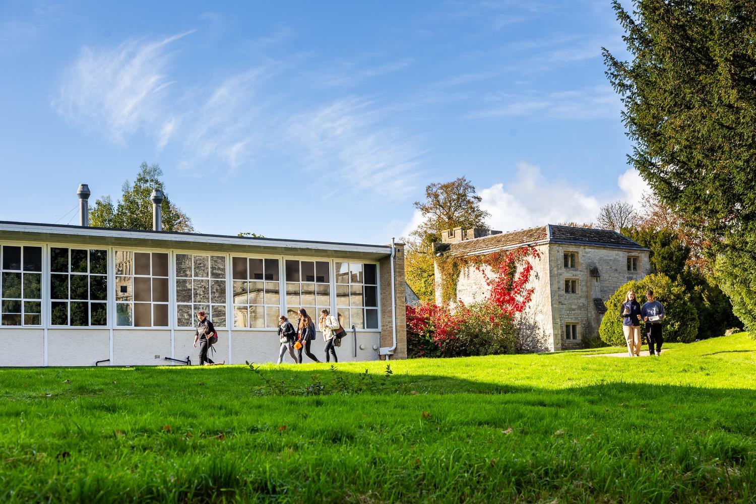 Two buildings surrounded by scenic green grass and trees, with students walking around